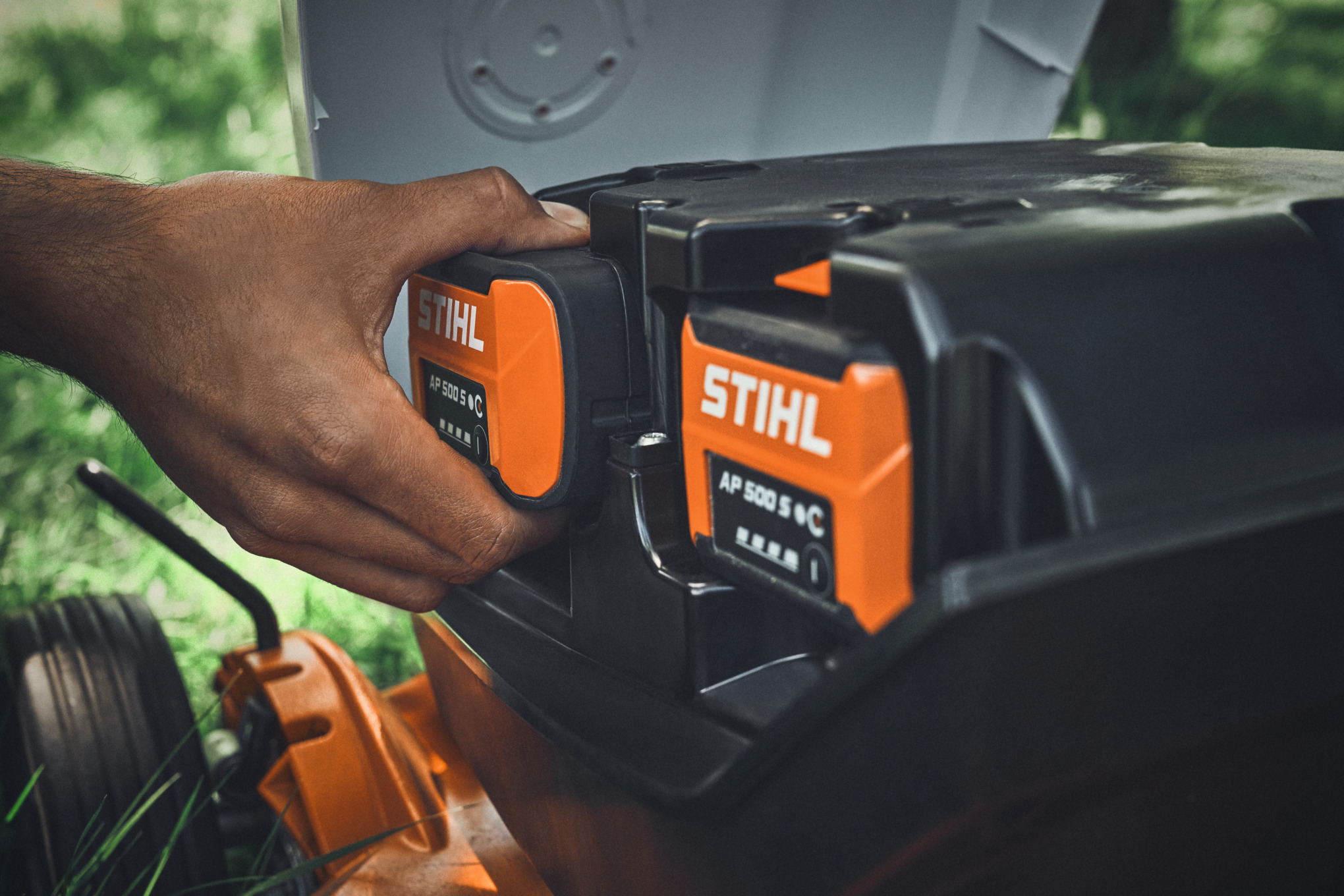 En person sætter et STIHL AP 500 S-batteri i en STIHL batteriplæneklipper