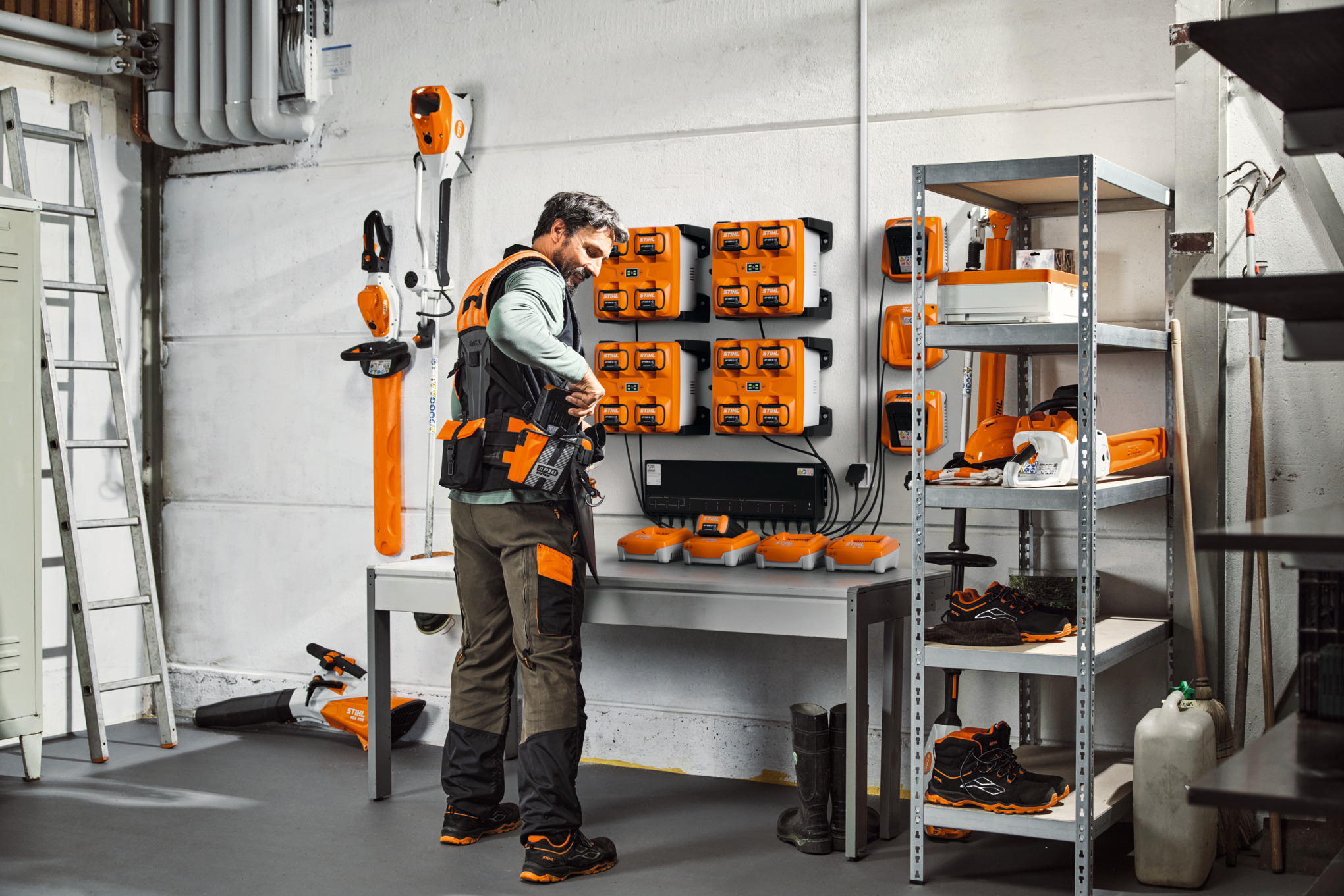 En mand i et opbevaringsrum med STIHL-enheder og batterier bærer STIHL ADVANCE X-Flex modulære bæltesystem