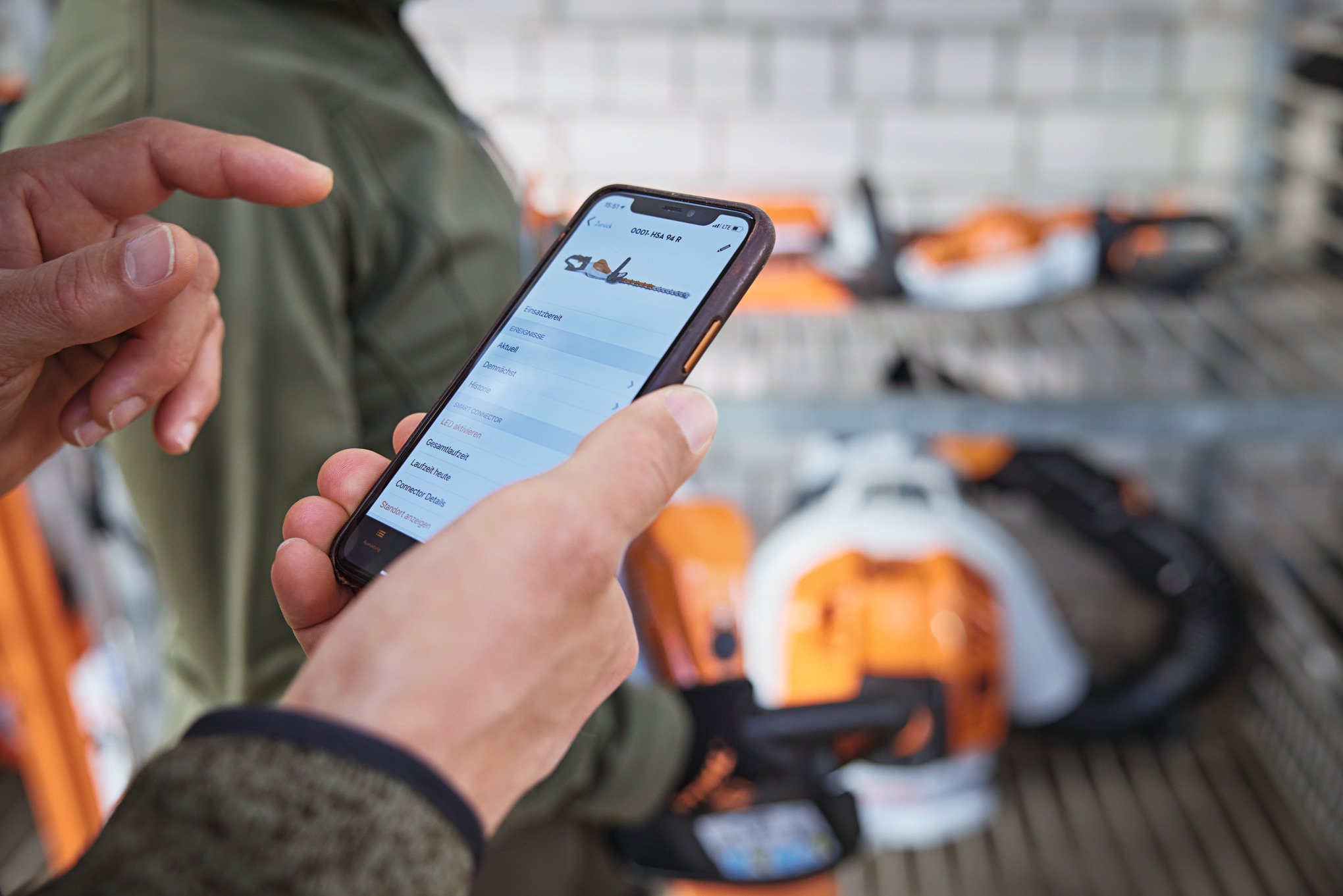 En person med en smartphone kigger på en motorsav i STIHL connected-appen