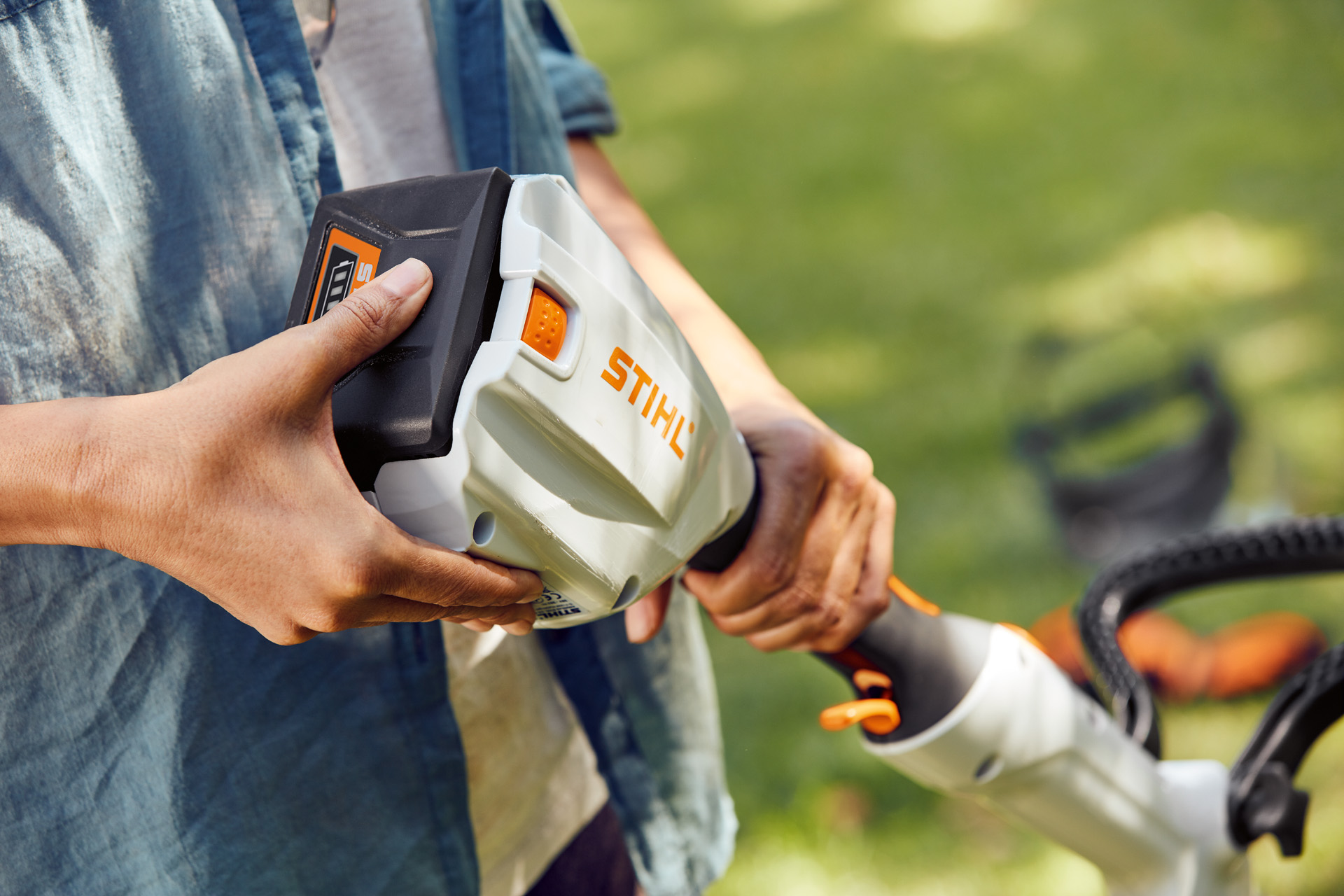 En person holder den batteridrevne STIHL trimmer FSA 56 i hånden og stryger hen over batteriet