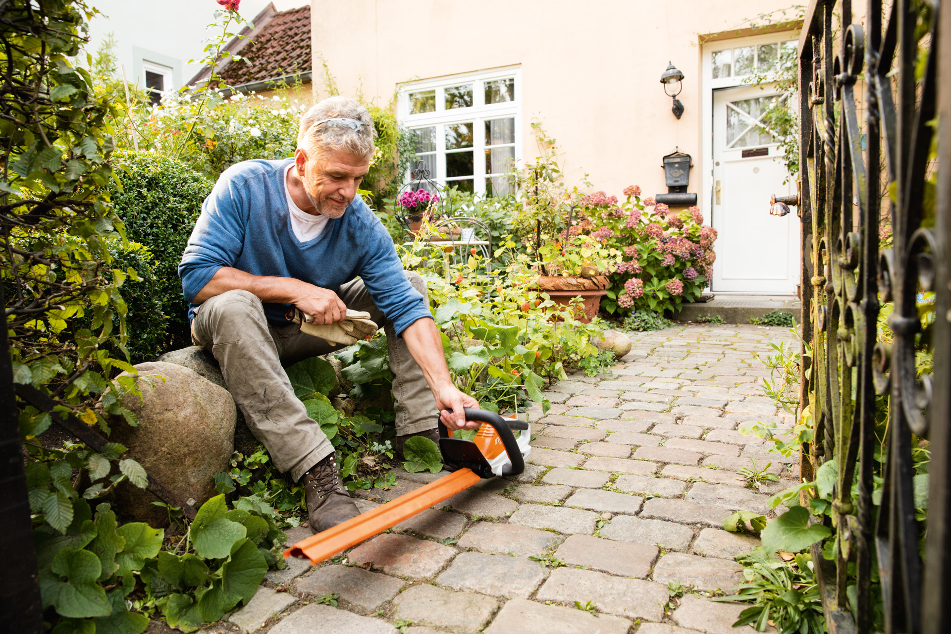 En mand med en elektrisk hækkeklipper STIHL HSA 45 i AI-serien foran et hus