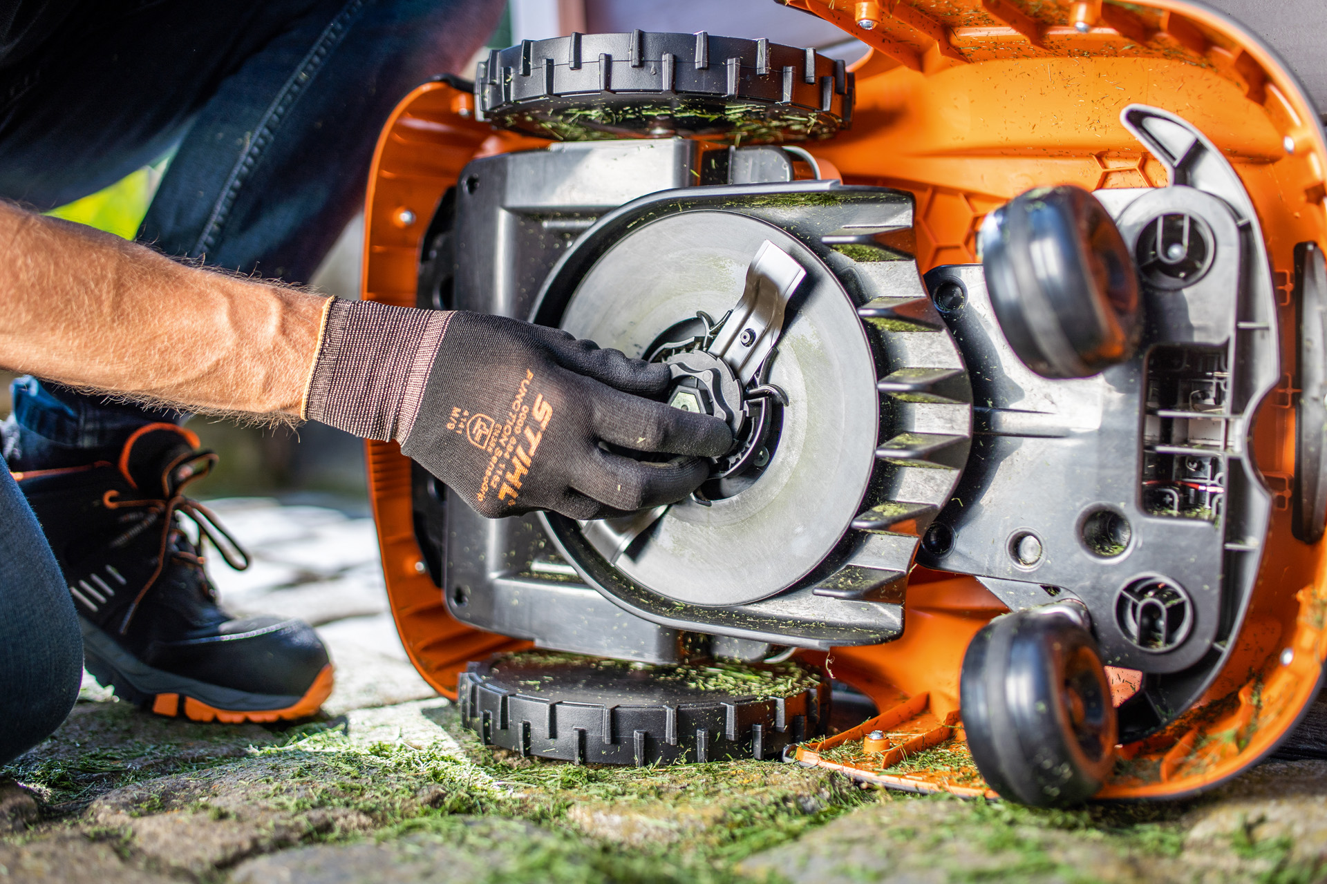 Et kig på den rene underside af en STIHL iMOW® robotplæneklipper, mens en person med handsker kontrollerer klingen.