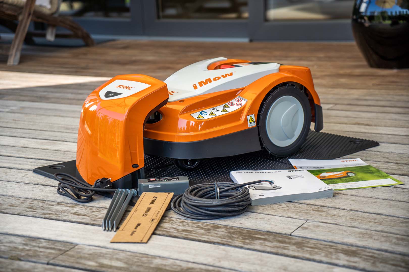 En STIHL iMOW® 422 robotplæneklipper på terrasse med kabel og betjeningsvejledning