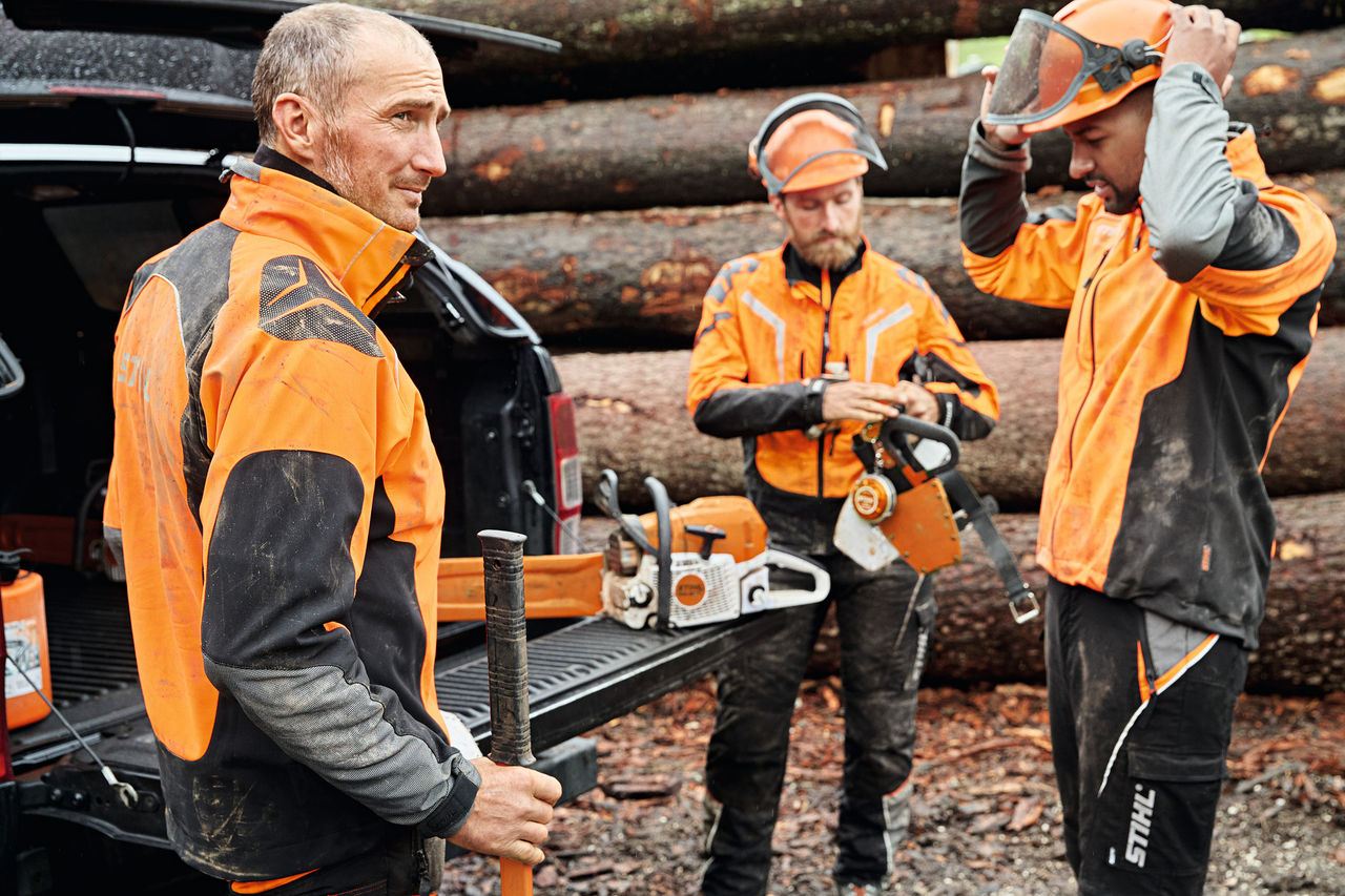 Tre mænd iført personligt beskyttelsesudstyr fra STIHL ved siden af et køretøj med åben bagagerumsklap