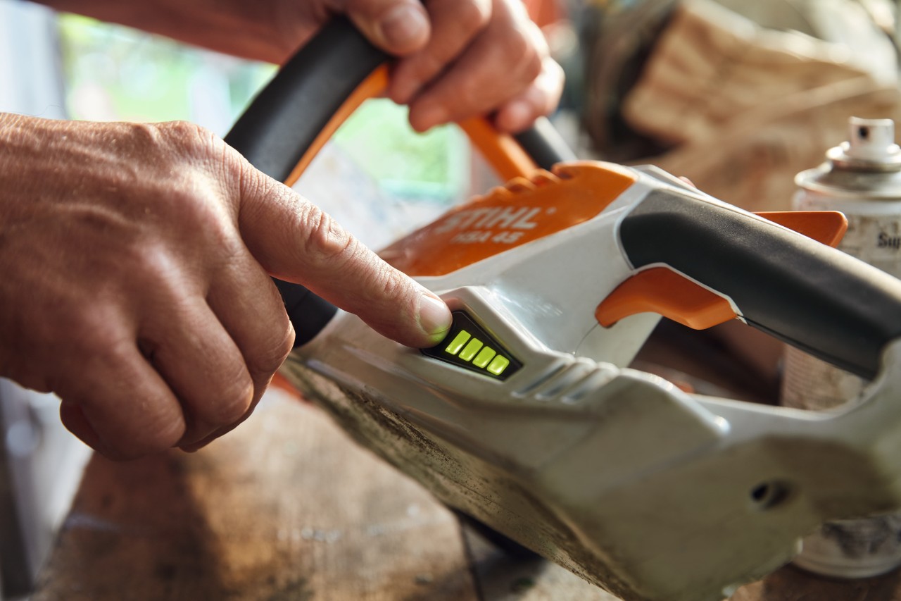En person kontrollerer opladningsniveauet på den batteridrevne hækklipper STIHL HSA 45.
