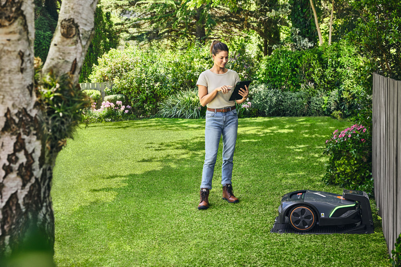 En kvinde, der betjener STIHL iMOW® EVO i sin have med en tablet